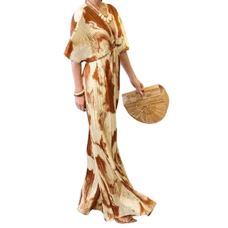 A woman modeling a long, flowing kimono-style dress with a brown and beige abstract tie-dye pattern, holding a round woven straw clutch against a light gray studio background.
