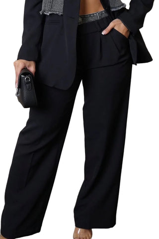 A person wearing black wide-leg trousers with a matching black blazer, holding a small black textured clutch against a textured neutral studio backdrop.