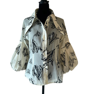 A cream-colored blouse with a black abstract floral pattern, displayed on a black mannequin torso against a plain white background.
